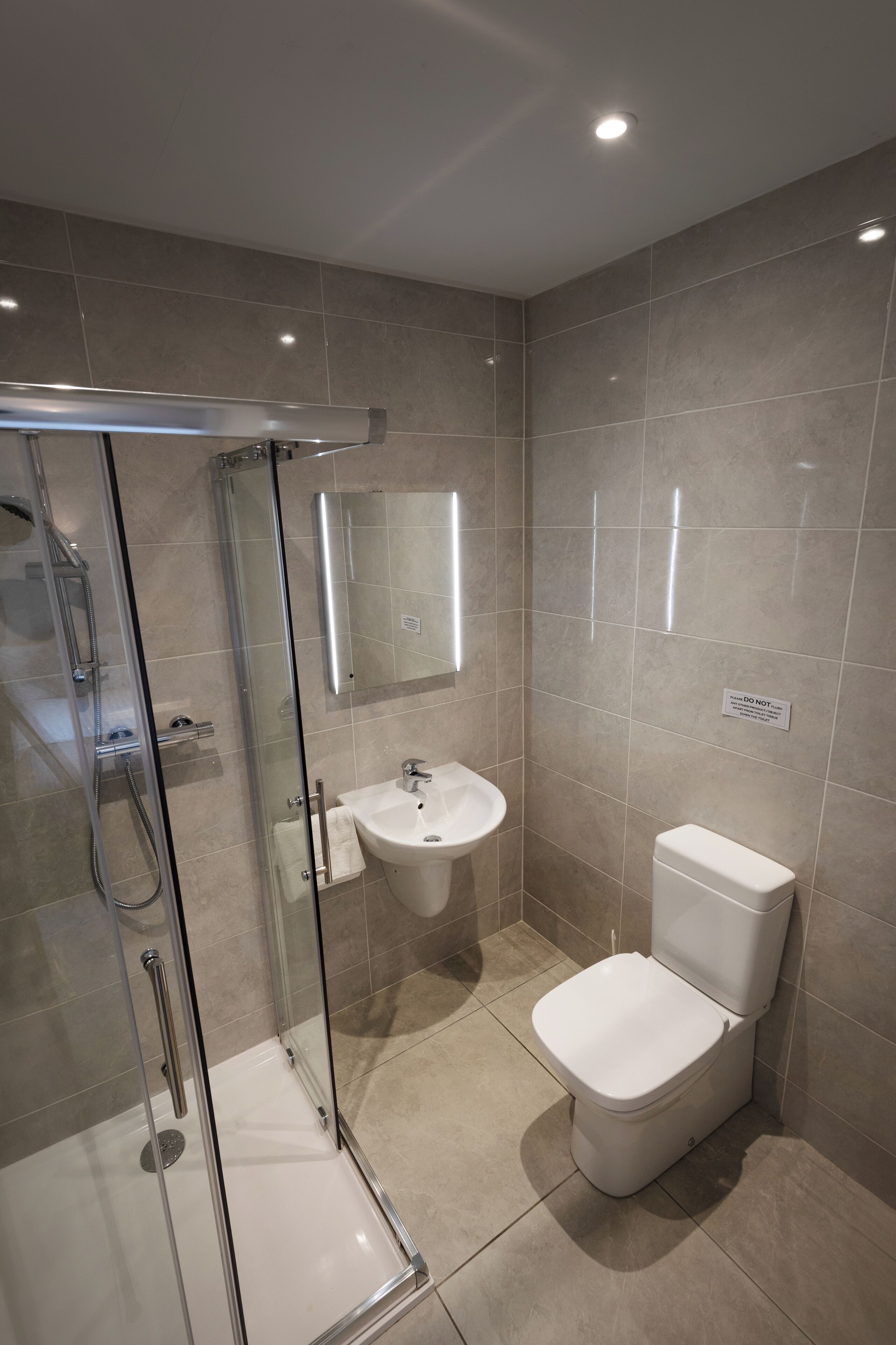 Un baño moderno con cabina de ducha de vidrio, un lavamanos blanco y un inodoro.