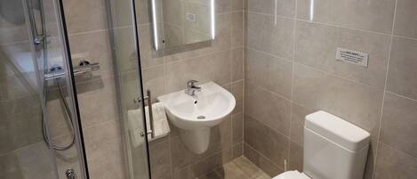 Un baño moderno con cabina de ducha de vidrio, un lavamanos blanco y un inodoro.