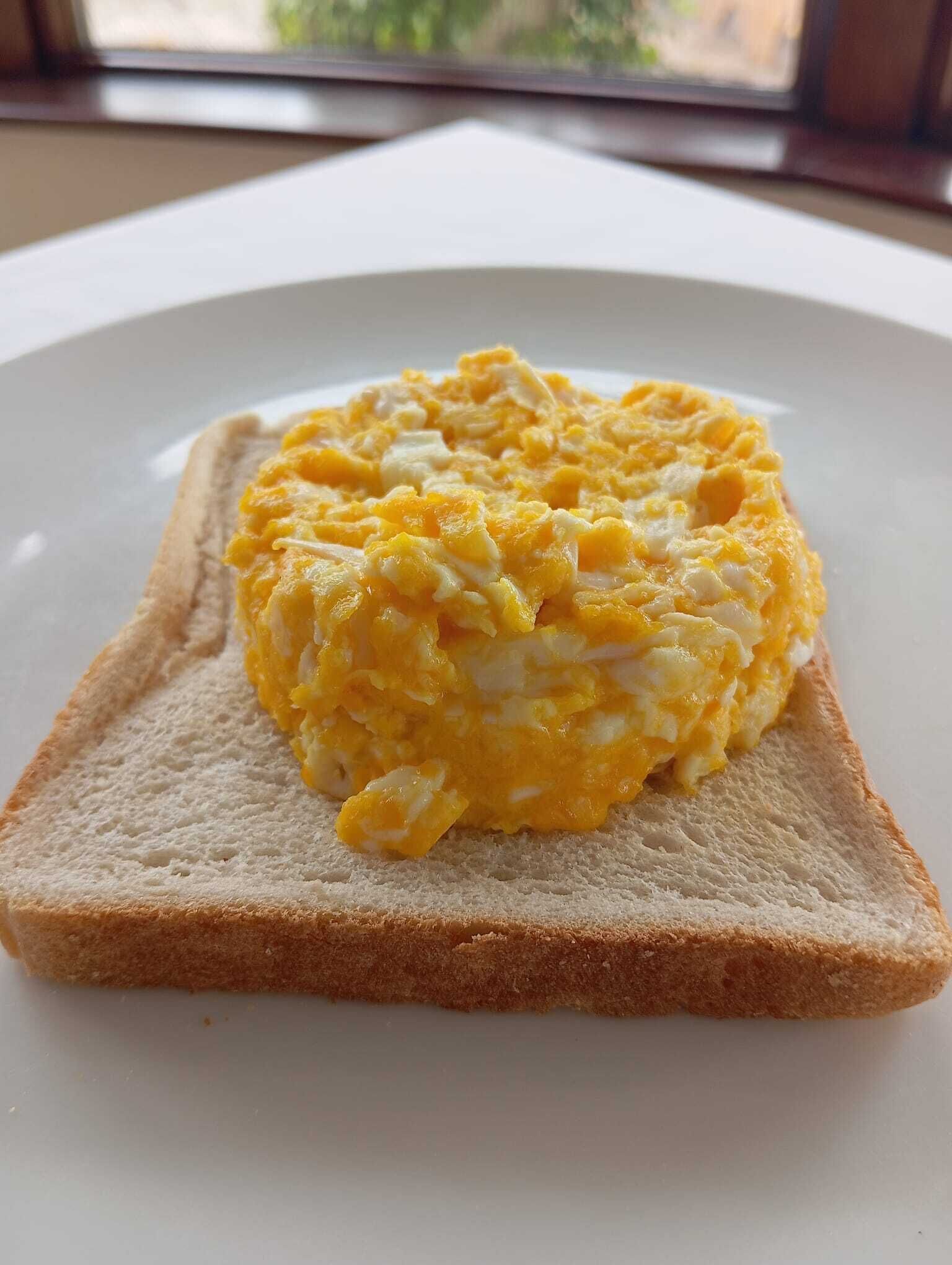 Una tostada con huevos revueltos sobre un plato blanco.
