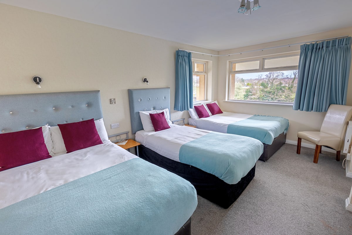 A hotel room with three beds, a chair, and a window with curtains.