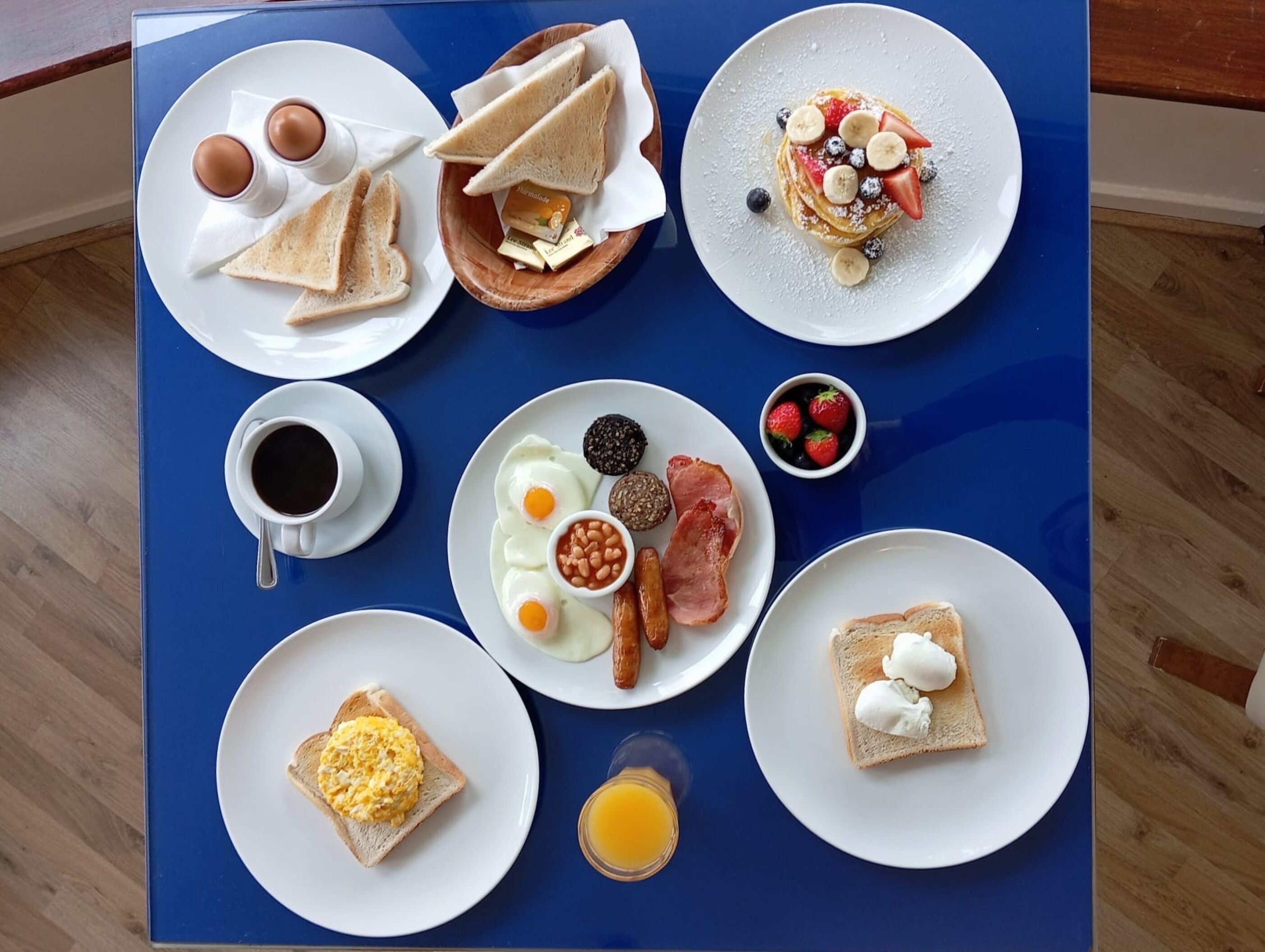 Una mesa azul con una variedad de platos para el desayuno, incluyendo tostadas, huevos, tocino y fruta.