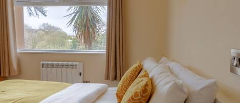 Ein Hotelzimmer mit einem Bett, einem Fenster mit Vorhängen, einem Heizkörper und einer Wandleuchte.