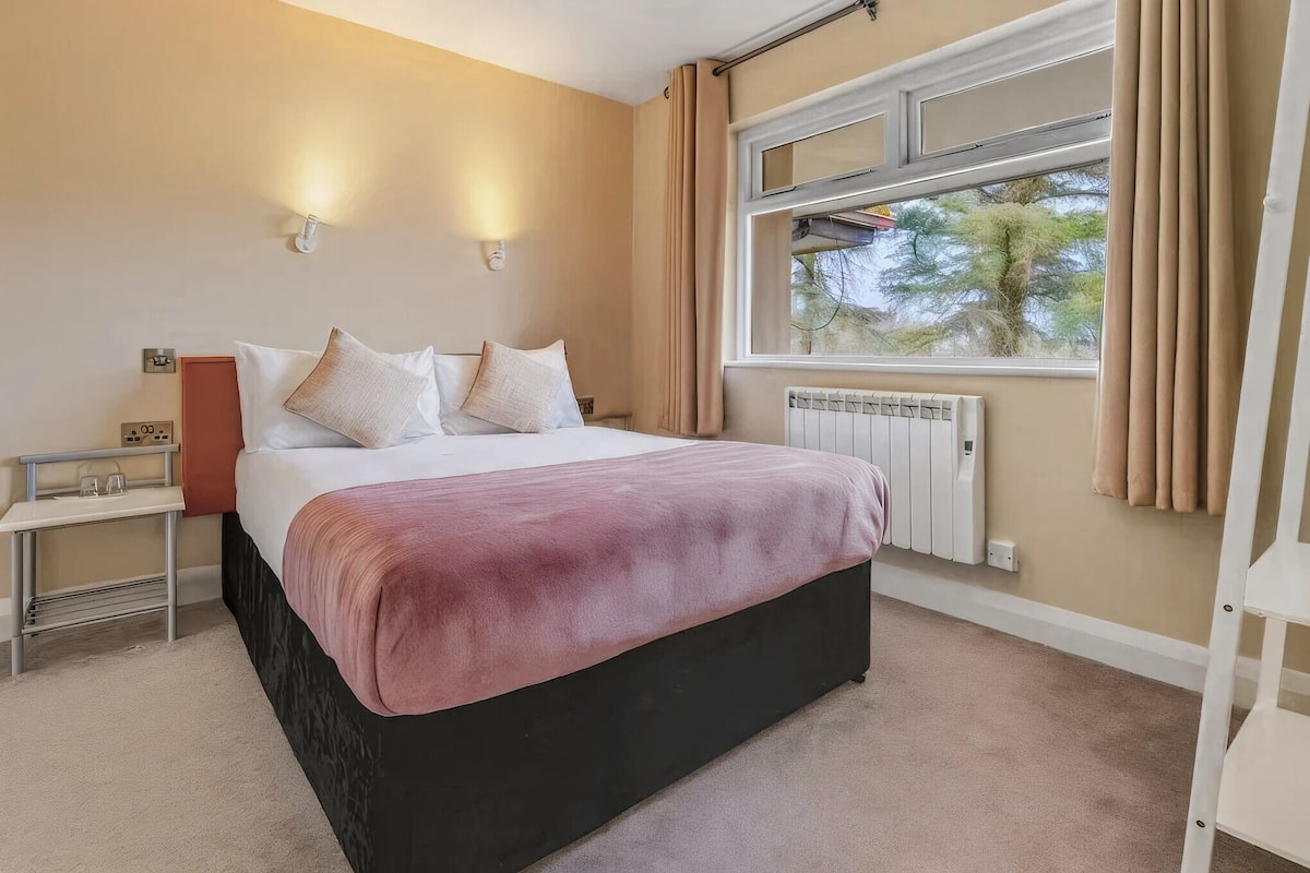 A bedroom with a bed, bedside tables, a window with curtains, and a radiator.