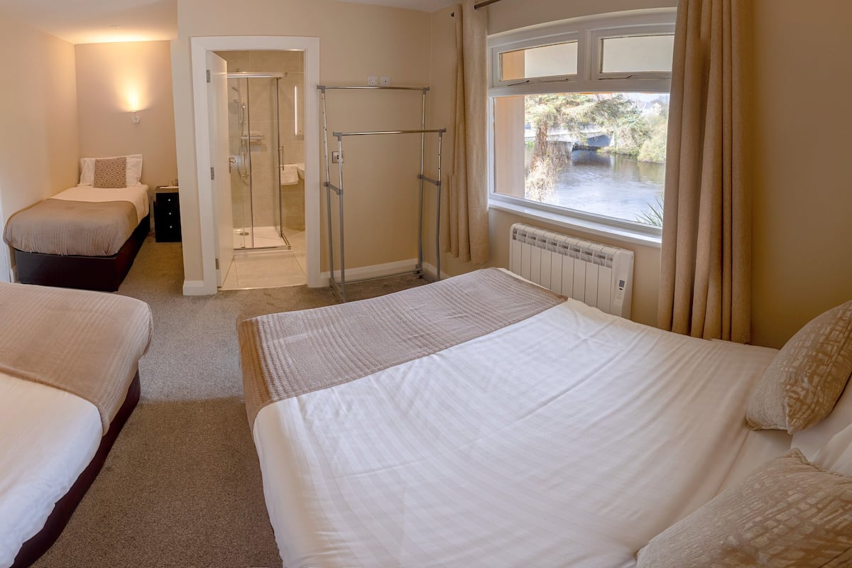 A hotel room with two beds, a shower area, and a window with a view of a river.