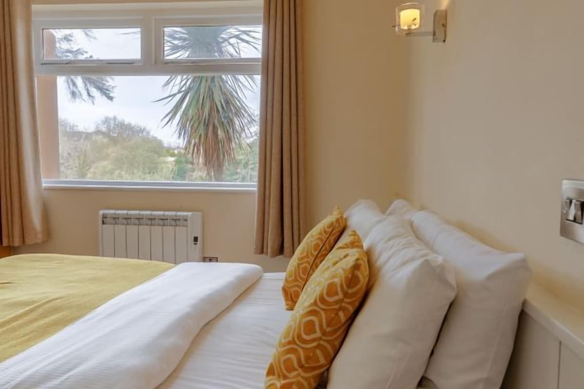 A hotel room with a bed, a window with curtains, a radiator, and a wall-mounted light fixture.