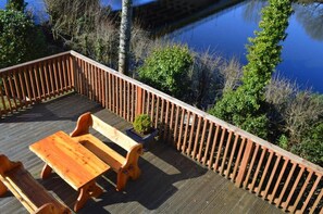 Une terrasse en bois, agrémentée d’une table et de bancs, entourée d’une balustrade en bois, et offrant une vue sur une étendue d’eau.