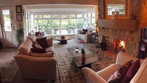 A cozy living room with a fireplace, comfortable seating, and large windows overlooking a body of water. - Killarney View House B&B (Killarney)