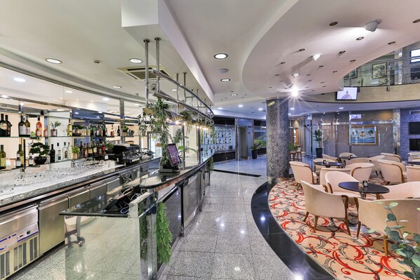 Zona de bar moderna con mostrador de vidrio, electrodomésticos de acero inoxidable y una variedad de botellas.