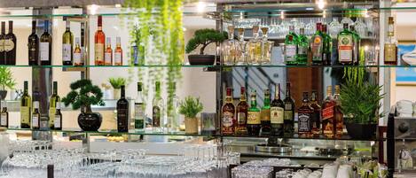 A bar area with shelves of liquor bottles, glasses, and decorative plants.
