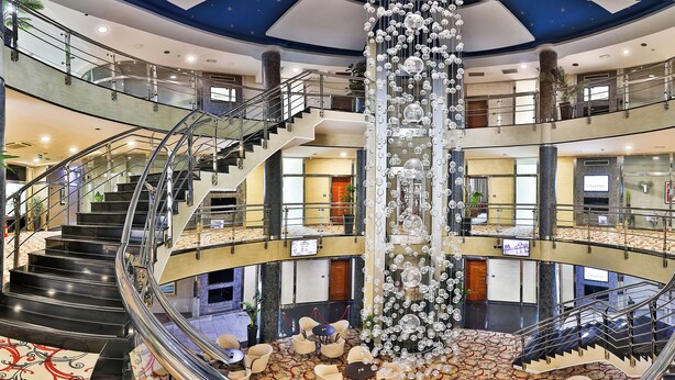 A multi-level atrium with a central decorative column, multiple staircases, and a patterned floor. - KINGS PARK HOTEL (Podgorica)