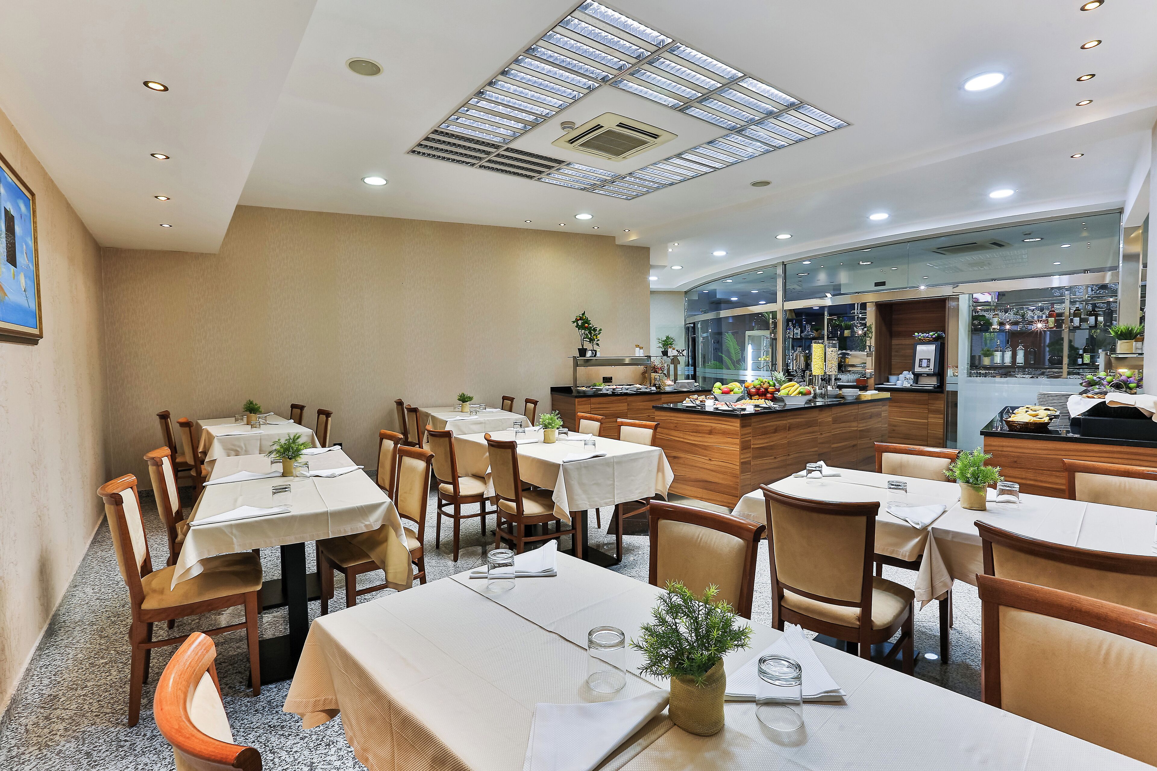 A restaurant with multiple tables and chairs, a counter with a display of food, and a skylight on the ceiling.