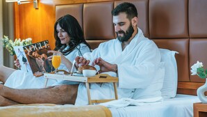 A couple in a hotel room reading a magazine, with a tray of breakfast including toast, a cup, and orange juice. - KINGS PARK HOTEL (Podgorica)
