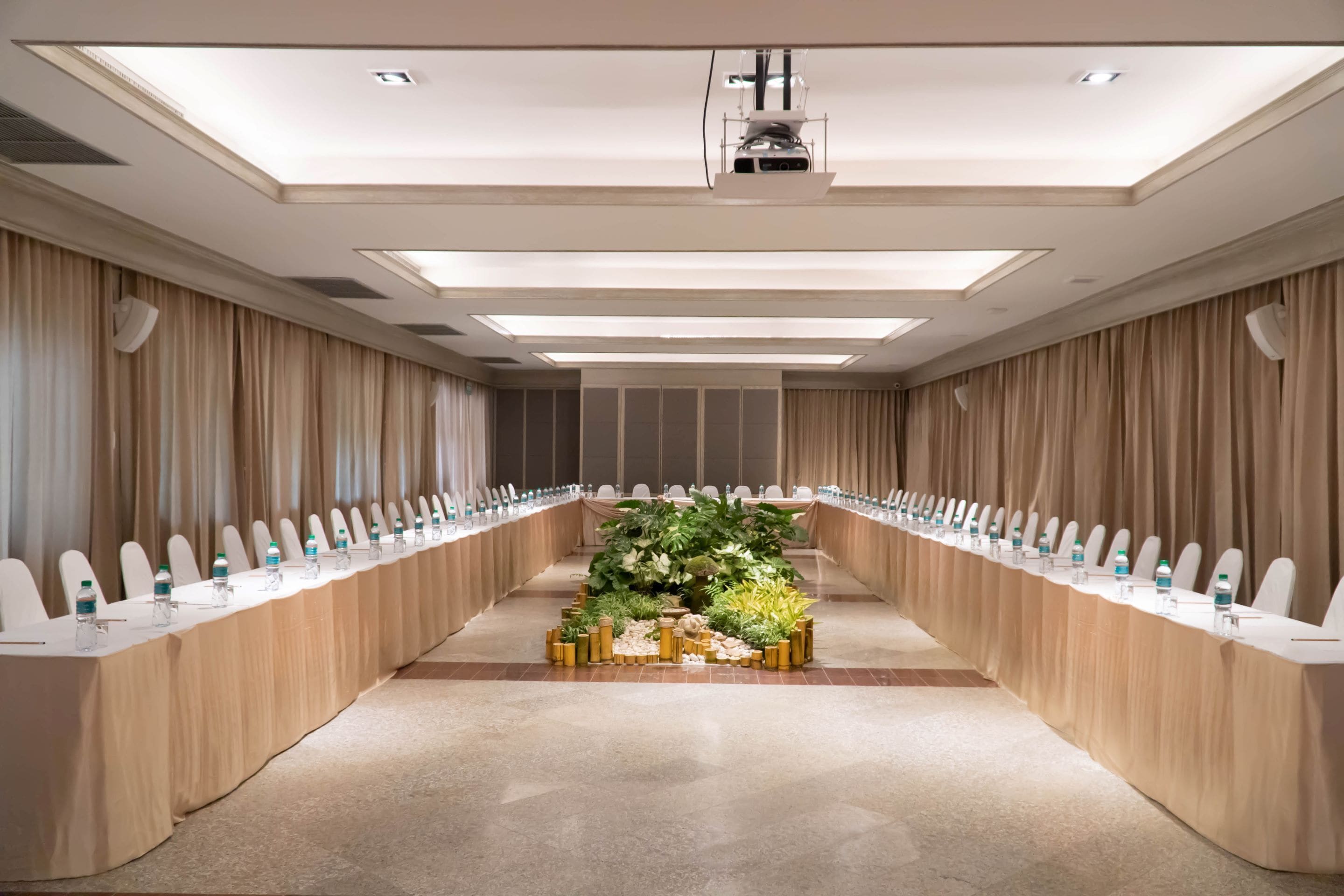 A conference room with a long table, chairs, and a projector on the ceiling.