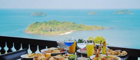 Una mesa con alimentos y bebidas para el desayuno, con vistas a un paisaje marino y varias islas.