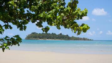Une plage à l’eau turquoise et limpide, un rivage sablonneux et, au loin, une île couverte de forêts.