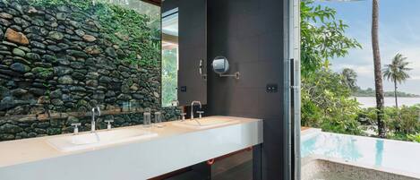 A modern bathroom with a stone wall, dual sinks, and a view of a pool.