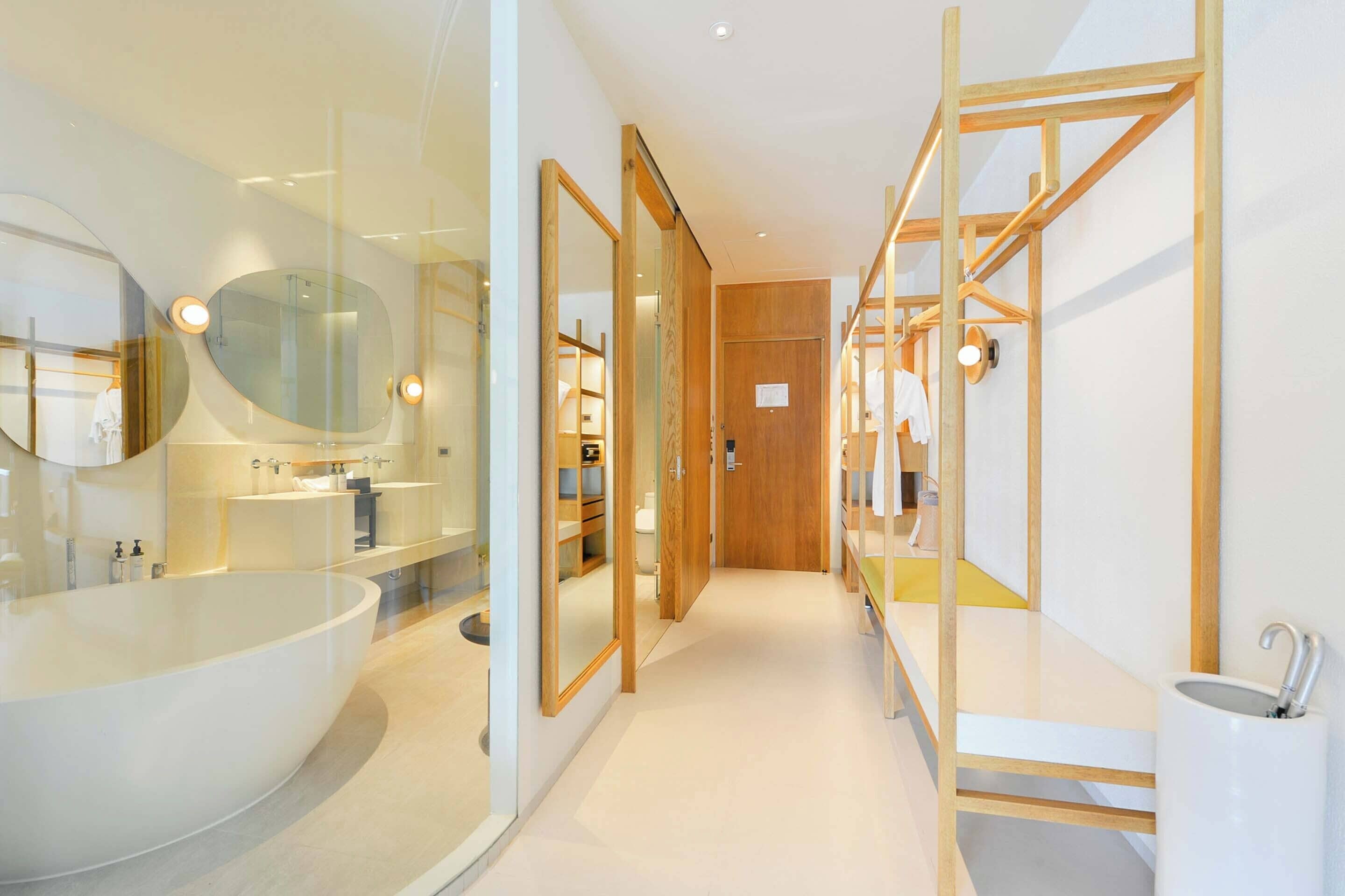 Un baño moderno con una bañera grande, ducha con mampara de vidrio, estanterías de madera y una puerta de madera.