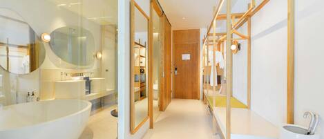 Un baño moderno con una bañera grande, ducha con mampara de vidrio, estanterías de madera y una puerta de madera.