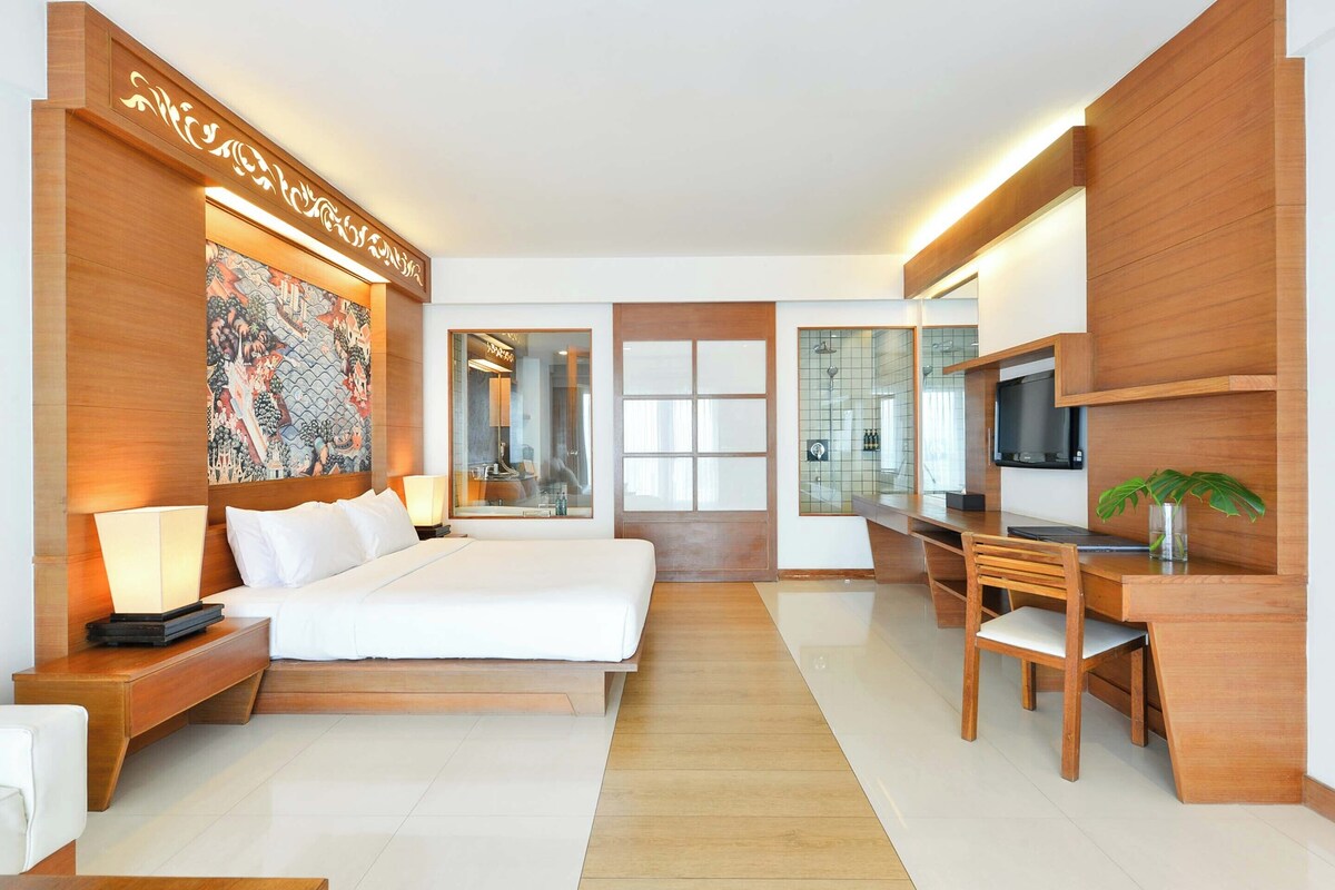 Een moderne hotelkamer met een groot bed, een bureau, een stoel, een televisie en een decoratief wandobject.