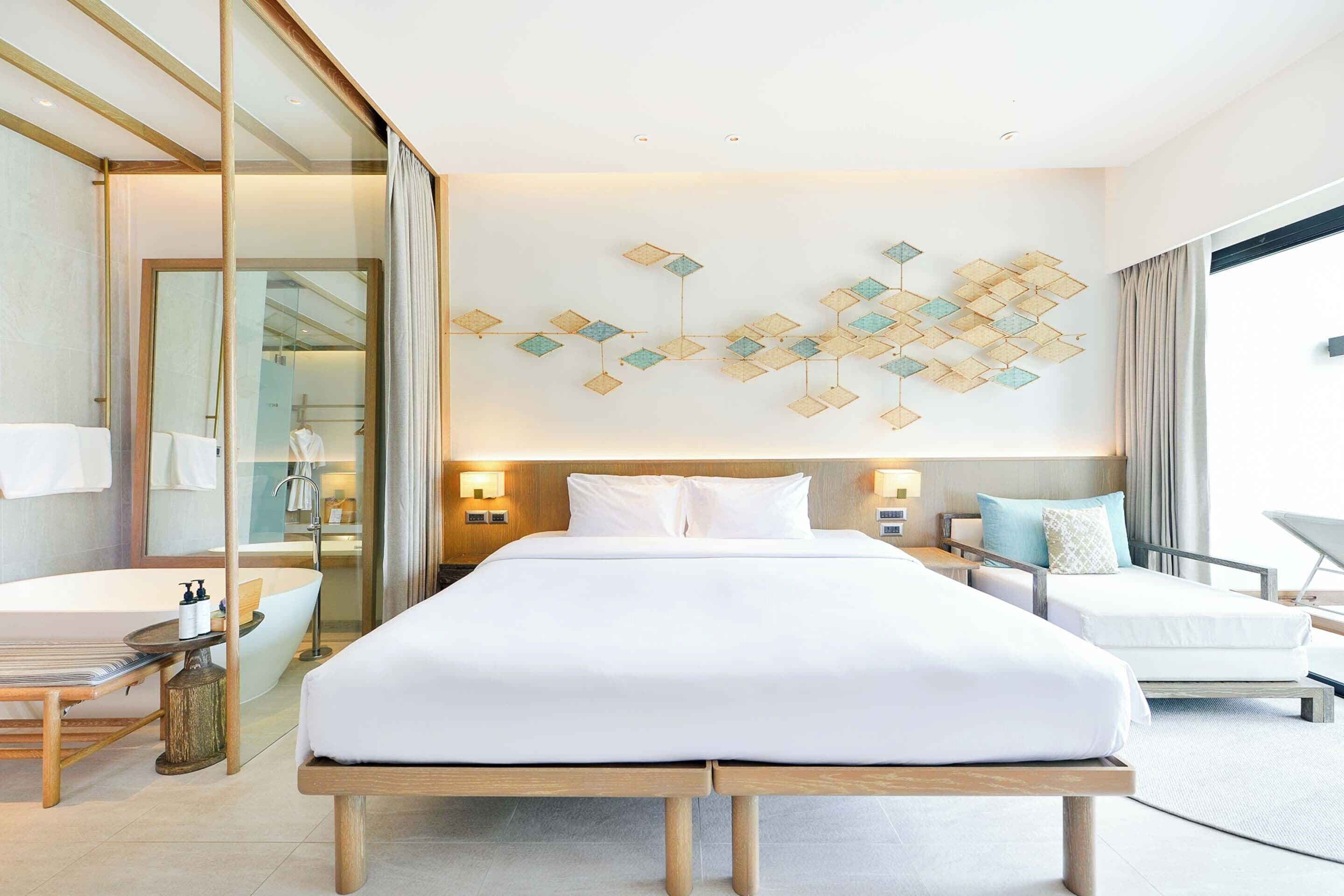 Habitación de hotel con una cama grande, zona de estar separada, bañera y un adorno en la pared.
