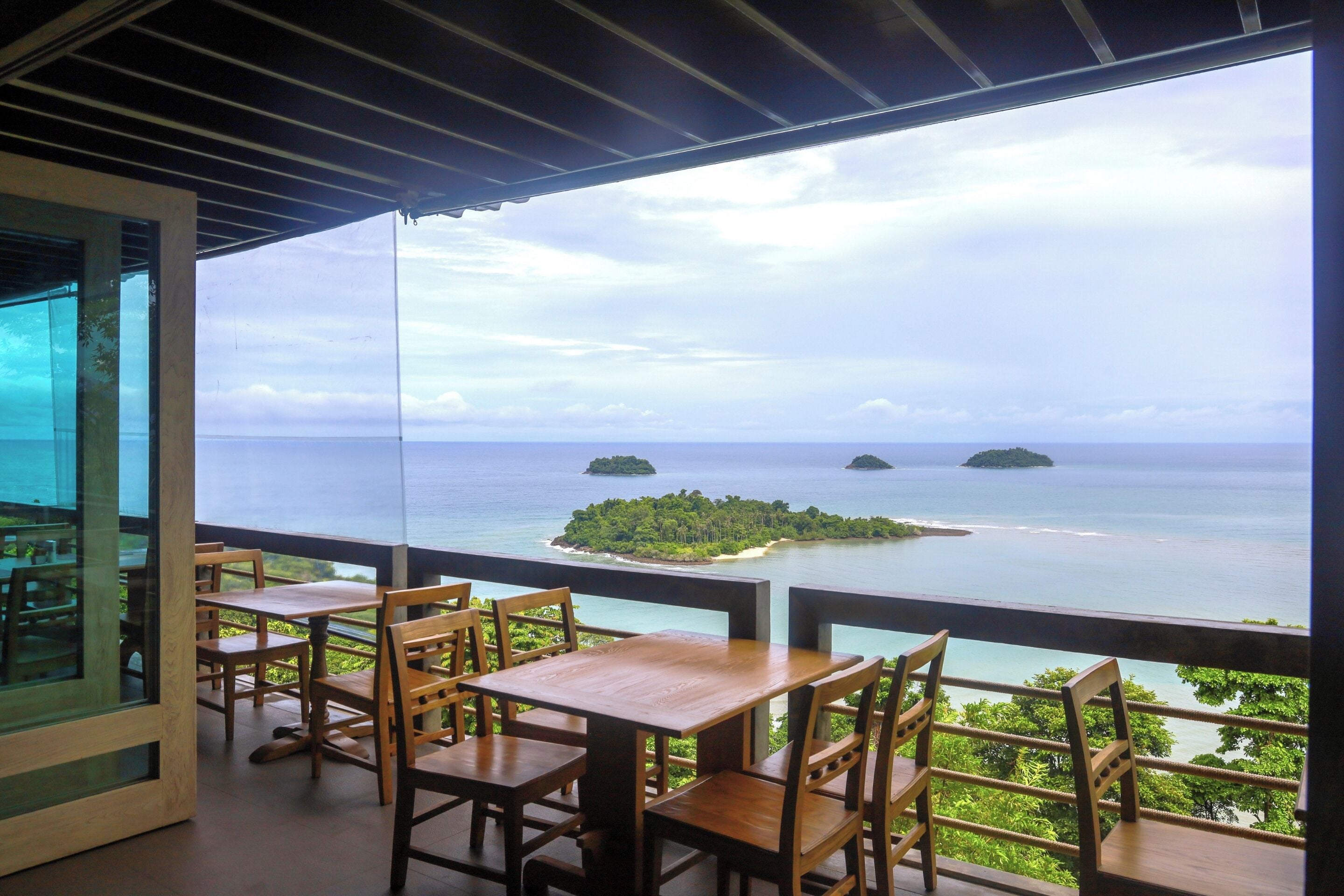 Una terraza con mesas y sillas de madera con vista al mar, islas y la costa.