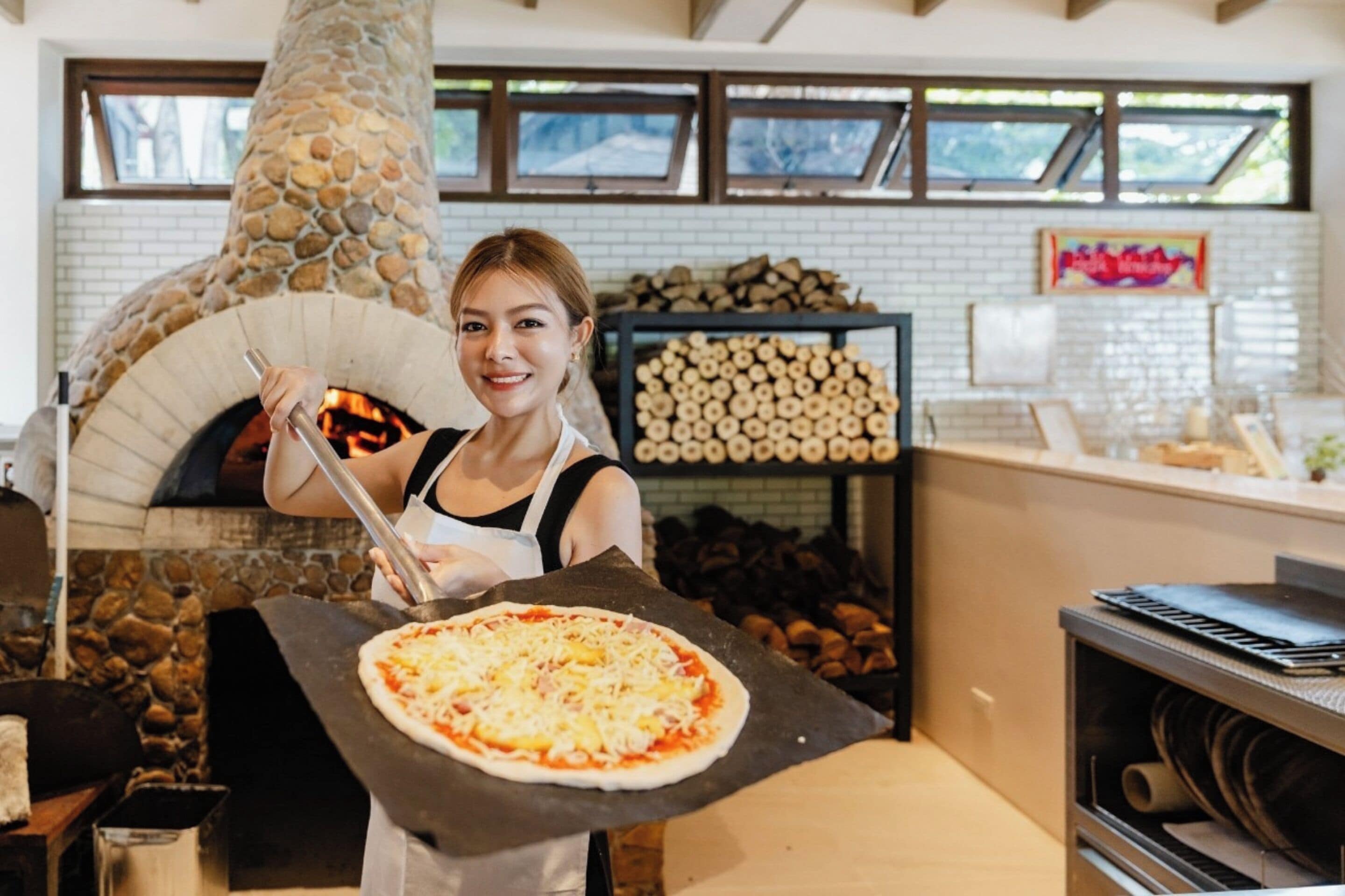A person holding a pizza in front of a stone oven.
