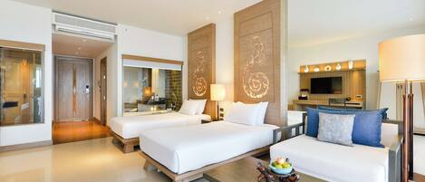 A hotel room with two beds, a sofa, a coffee table, a TV, and a bathroom visible in the background.