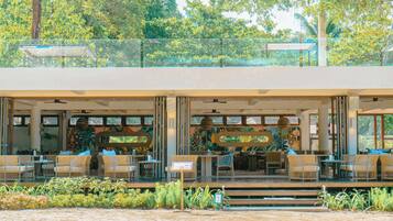 A beachfront restaurant with outdoor seating, a glass balustrade, and tropical murals.