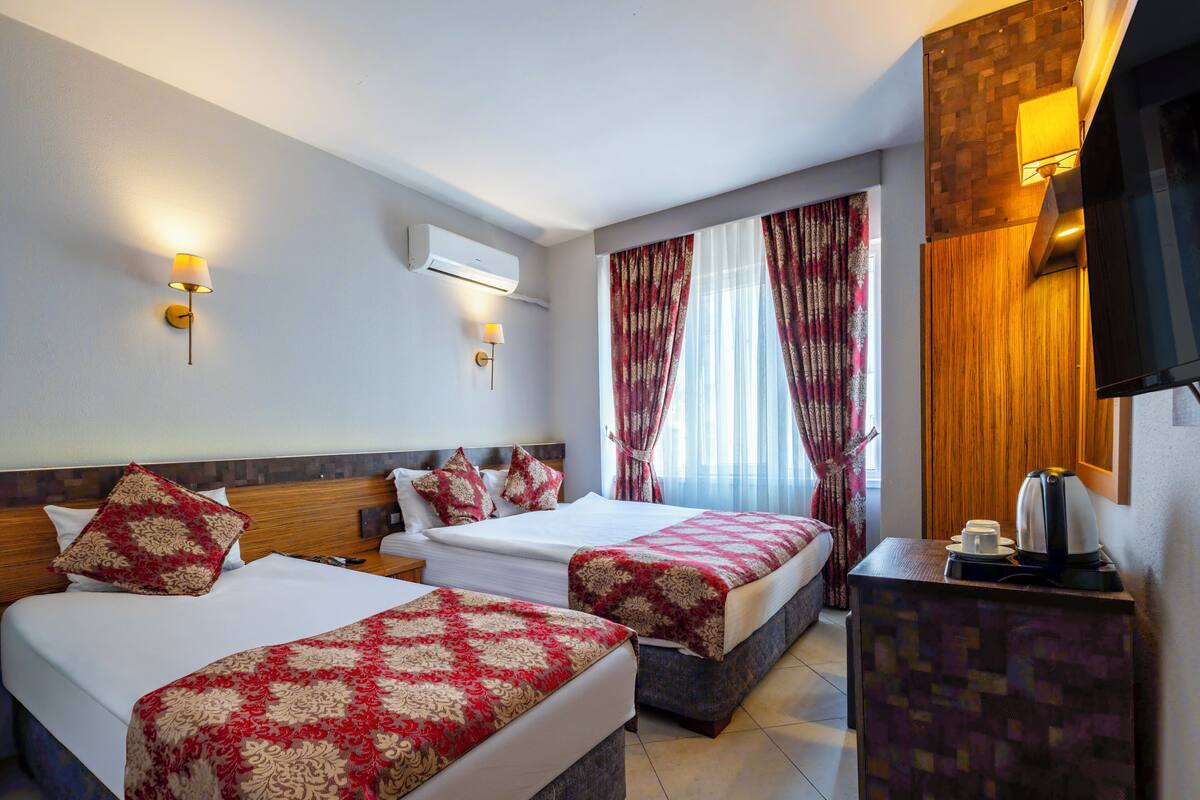 Habitación de hotel con dos camas, cafetera, aire acondicionado y televisor en la pared.