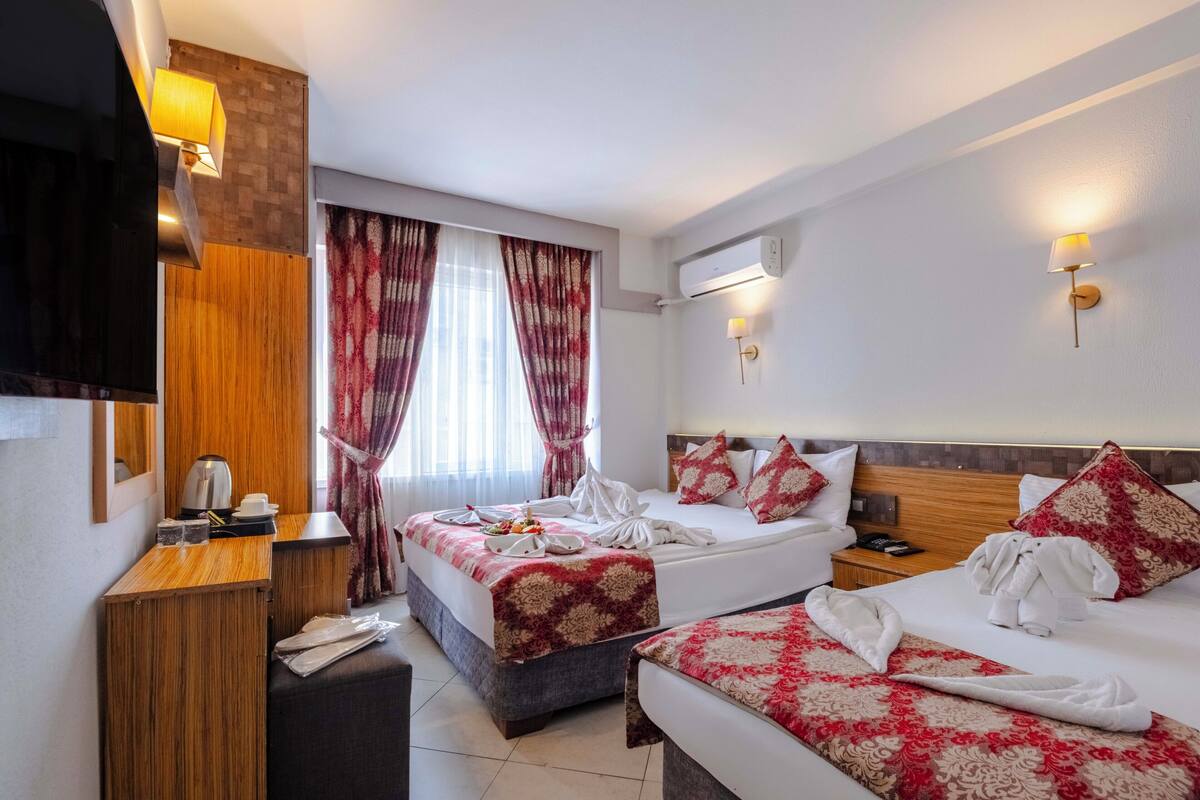 Habitación de hotel con dos camas, un escritorio de madera, un televisor y una ventana con cortinas.
