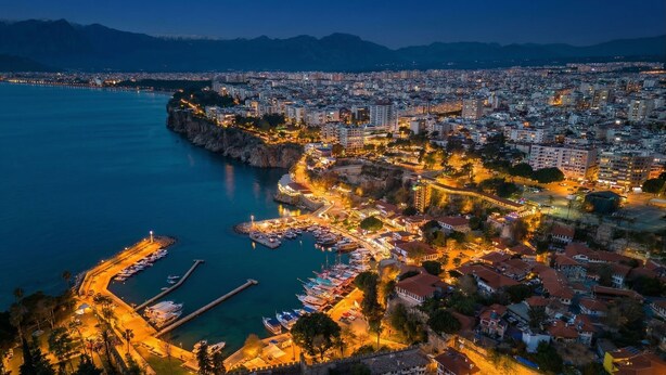 An aerial view of a coastal city with a marina, buildings, and a fortified area. - Hotel Mevre (Antalya)