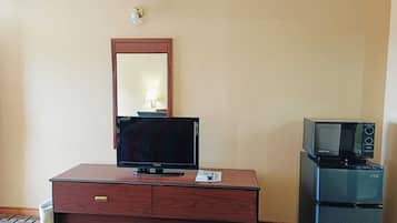 A hotel room with a wooden dresser, a flat-screen TV, a microwave, and a bed with a colorful quilt.