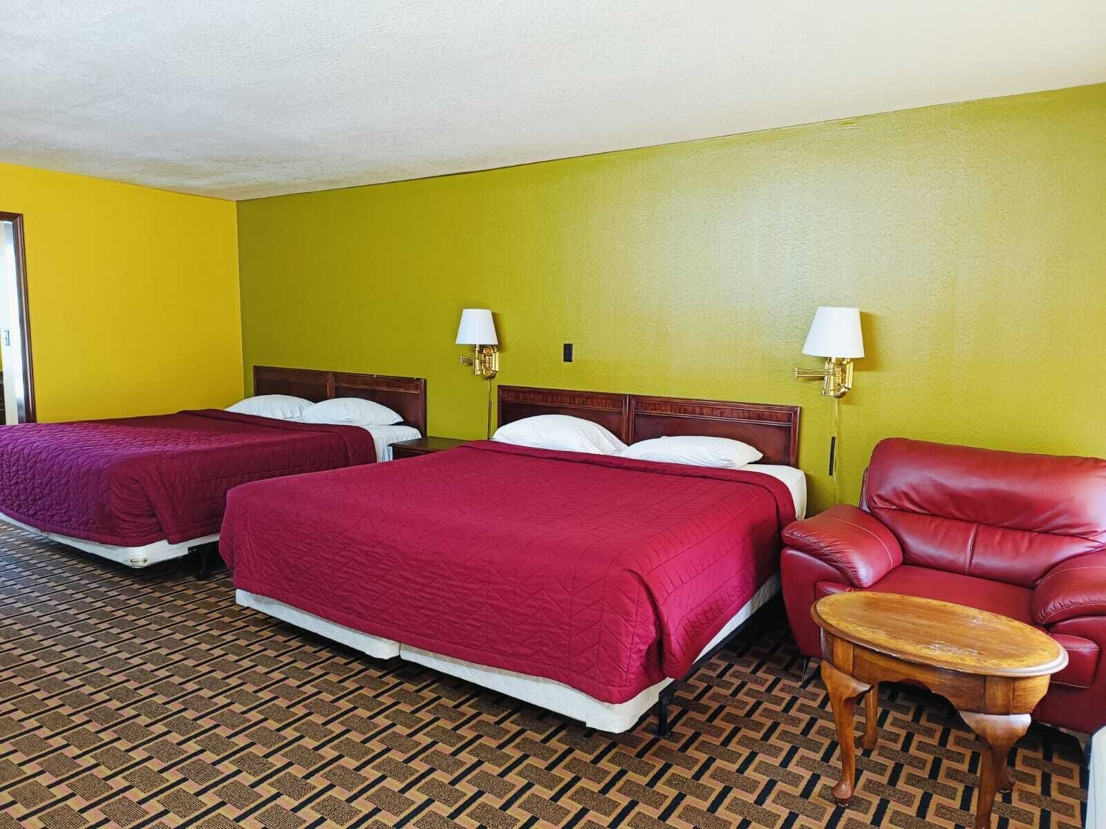 A hotel room with two beds, a red leather chair, and a small wooden table.