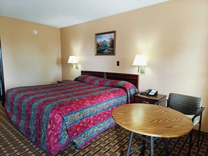 A hotel room with a large bed, two bedside lamps, a small round table, and a chair. - Victorian Inn (Athens)