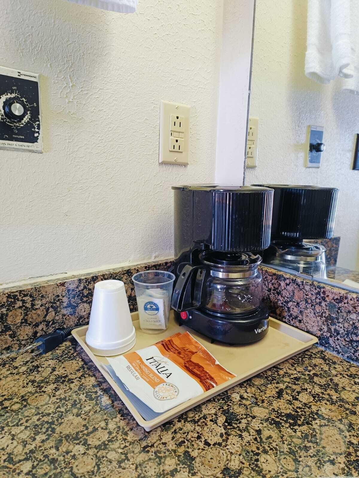 A kitchen counter with a coffee maker, a cup, a container of sugar, and a bag of coffee.