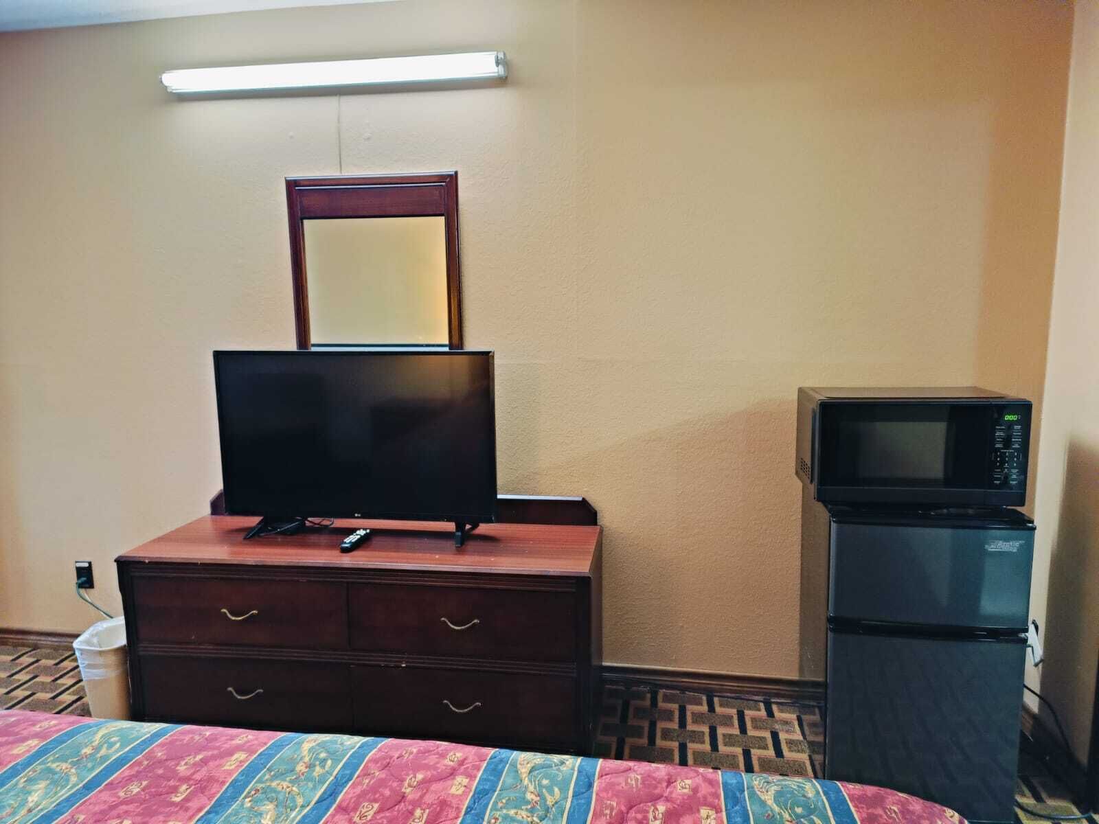 A hotel room with a TV on a dresser, a microwave, and a bed with a patterned bedspread.