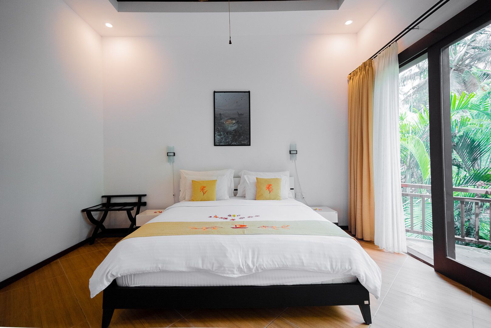 Un dormitorio moderno con una cama grande, una mesita pequeña y vistas a zonas verdes por la ventana.