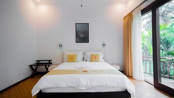 Un dormitorio moderno con una cama grande, una mesita pequeña y vistas a zonas verdes por la ventana.
