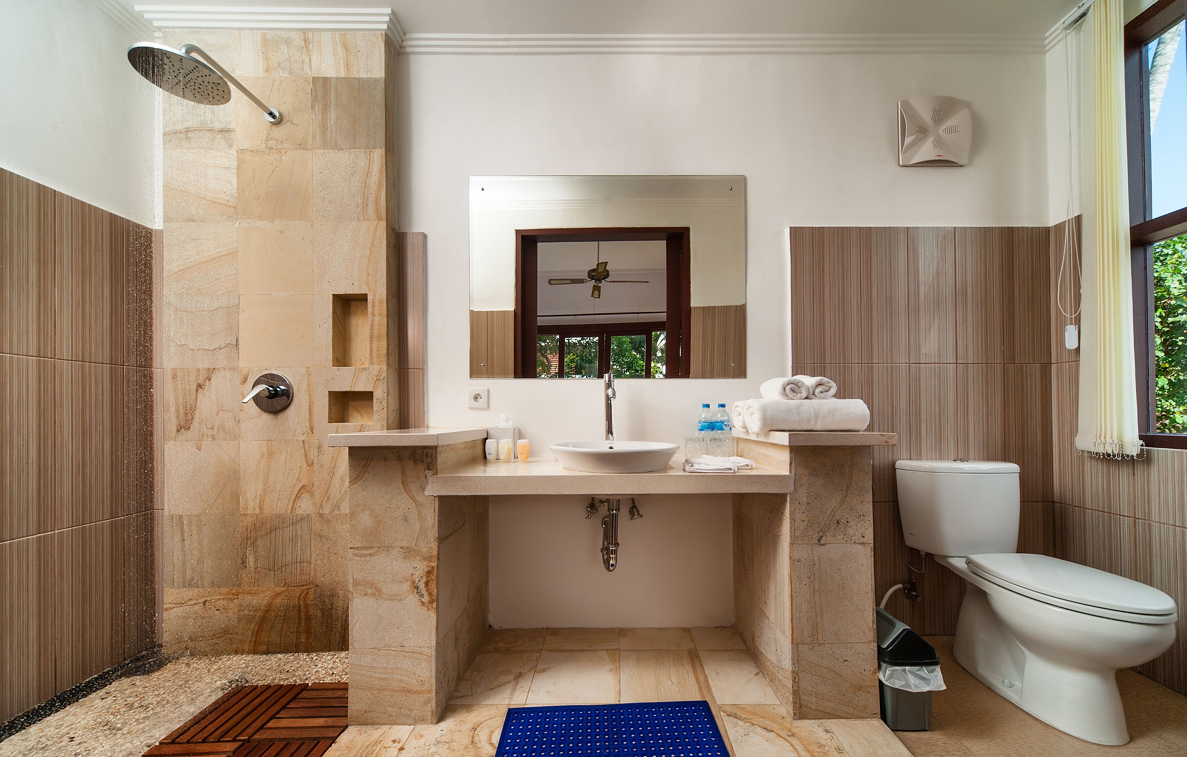 Ein Badezimmer mit Dusche, Waschbecken, Toilette und einem Fenster mit Blick auf Grünflächen.