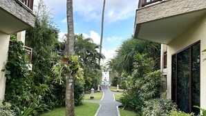 Ein Weg, gesäumt von üppiger Vegetation und Palmen, der zu einem Gebäude mit einem Balkon führt.