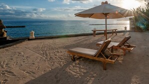 Eine Strandlounge mit Holzliegen und einem großen Sonnenschirm mit Blick auf das Meer.