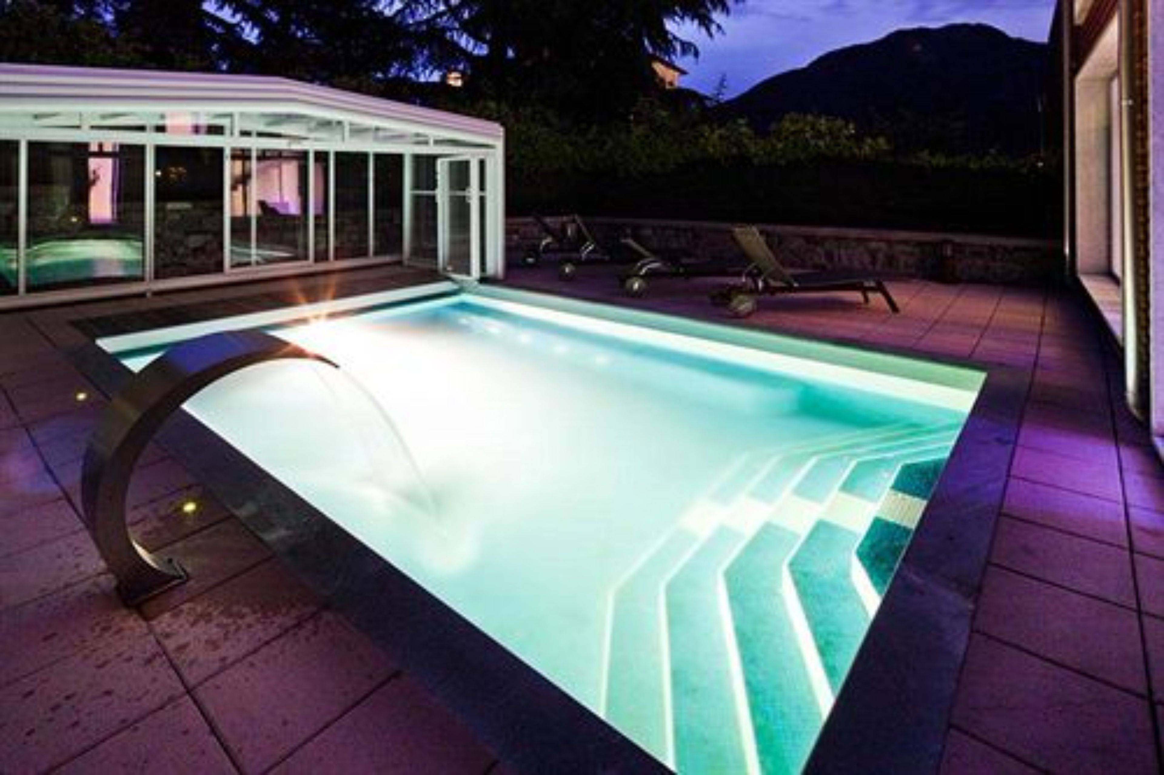 Ein Schwimmbecken mit Glasüberdachung und einer Steinsäule im Hintergrund.