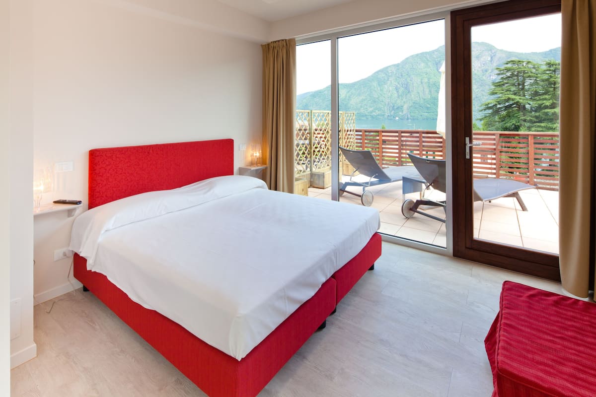 A hotel room with a large bed, a balcony with a view of mountains, and a red chair.