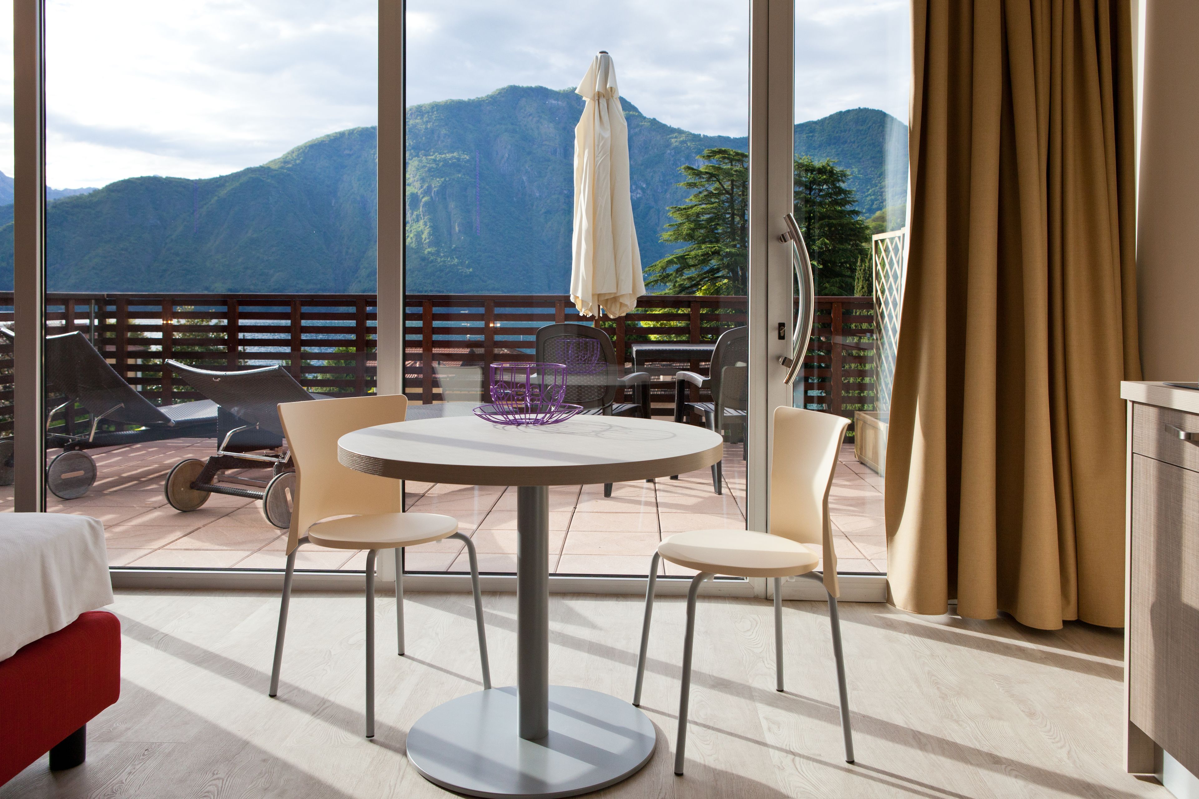 A balcony with a table and chairs, a white umbrella, and a view of mountains.