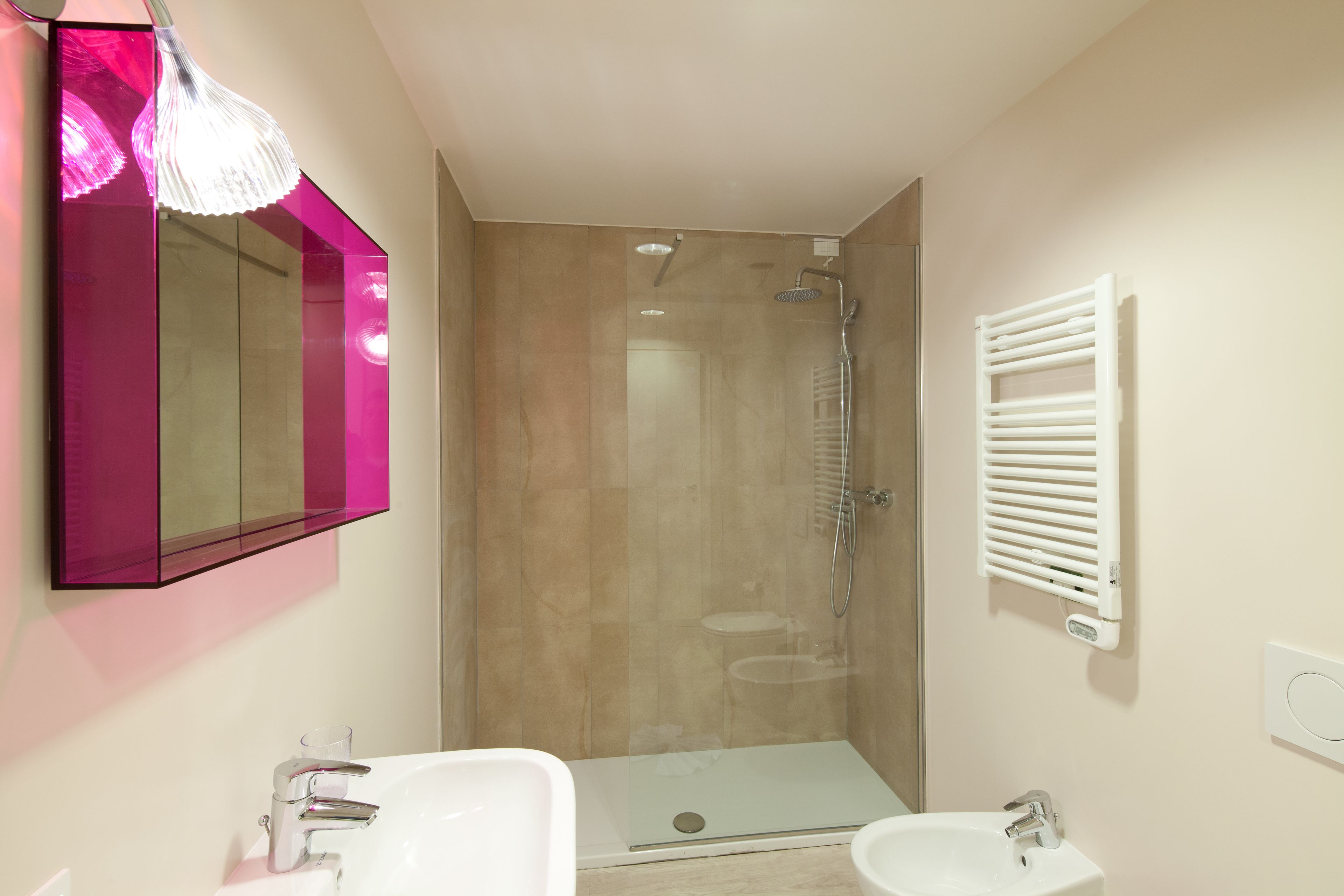 A modern bathroom with a glass shower enclosure, a white sink, and a mirror with a pink frame.