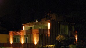 A modern building with a flat roof, large windows, and a well-lit facade at night. - Residence Lenno (Tremezzina)