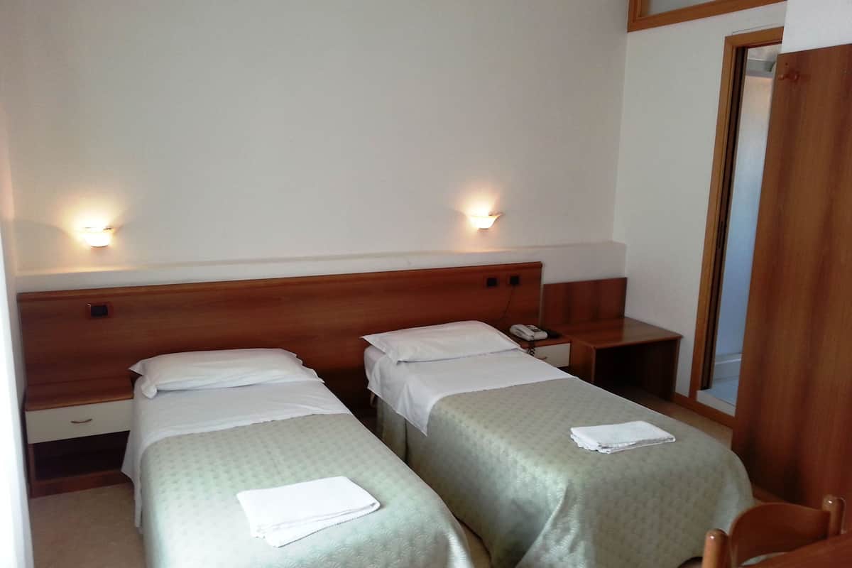 A hotel room with two single beds, a wooden headboard, bedside tables, a nightstand, a desk, and a mirror.