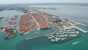An aerial view of a coastal city with a dense urban area, a marina, and a large body of water. - Hotel Clodia (Chioggia)