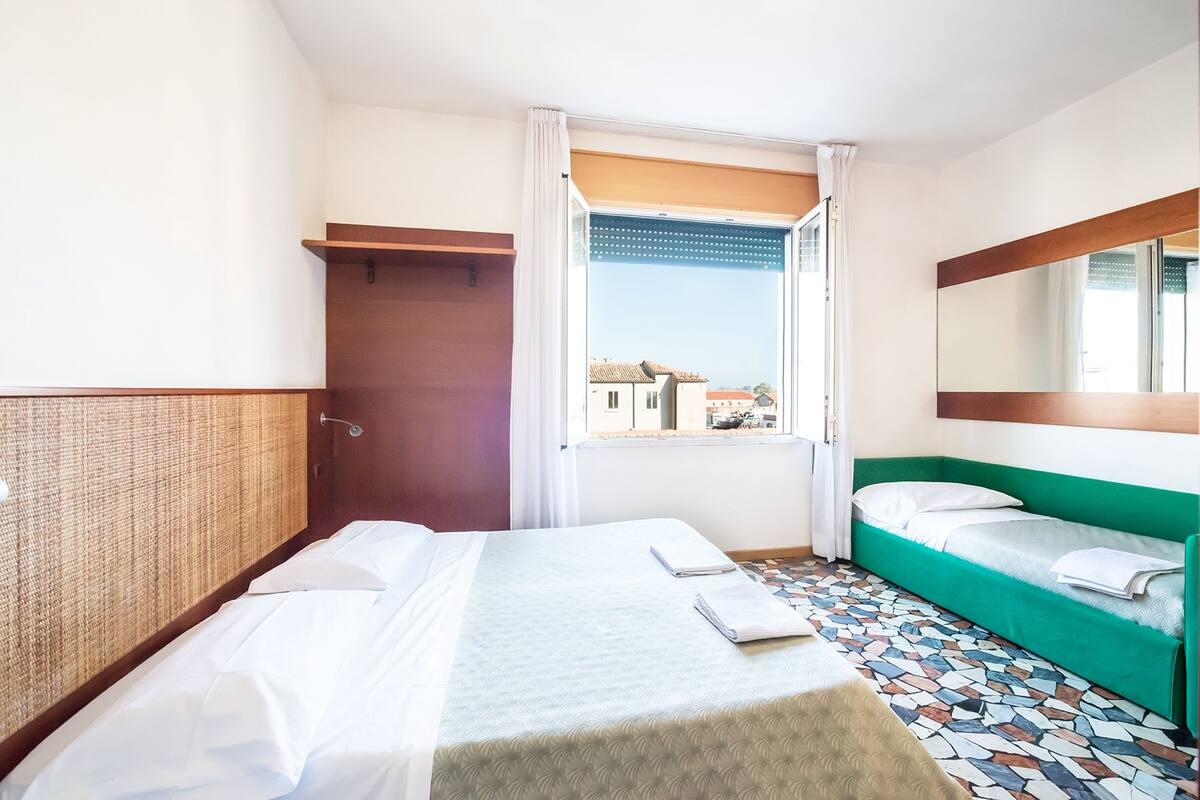 A hotel room with a bed, a sofa, a window with curtains, and a patterned floor.