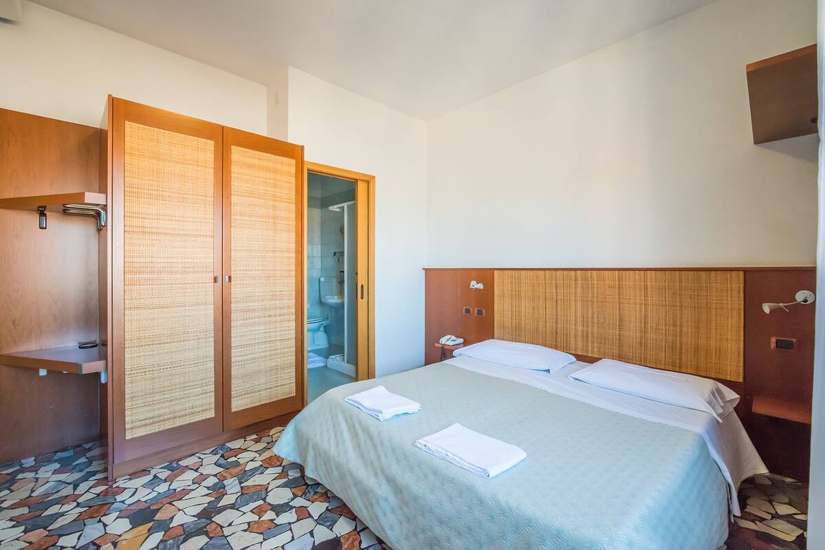 A hotel room with a bed, a wardrobe, and a shower area.